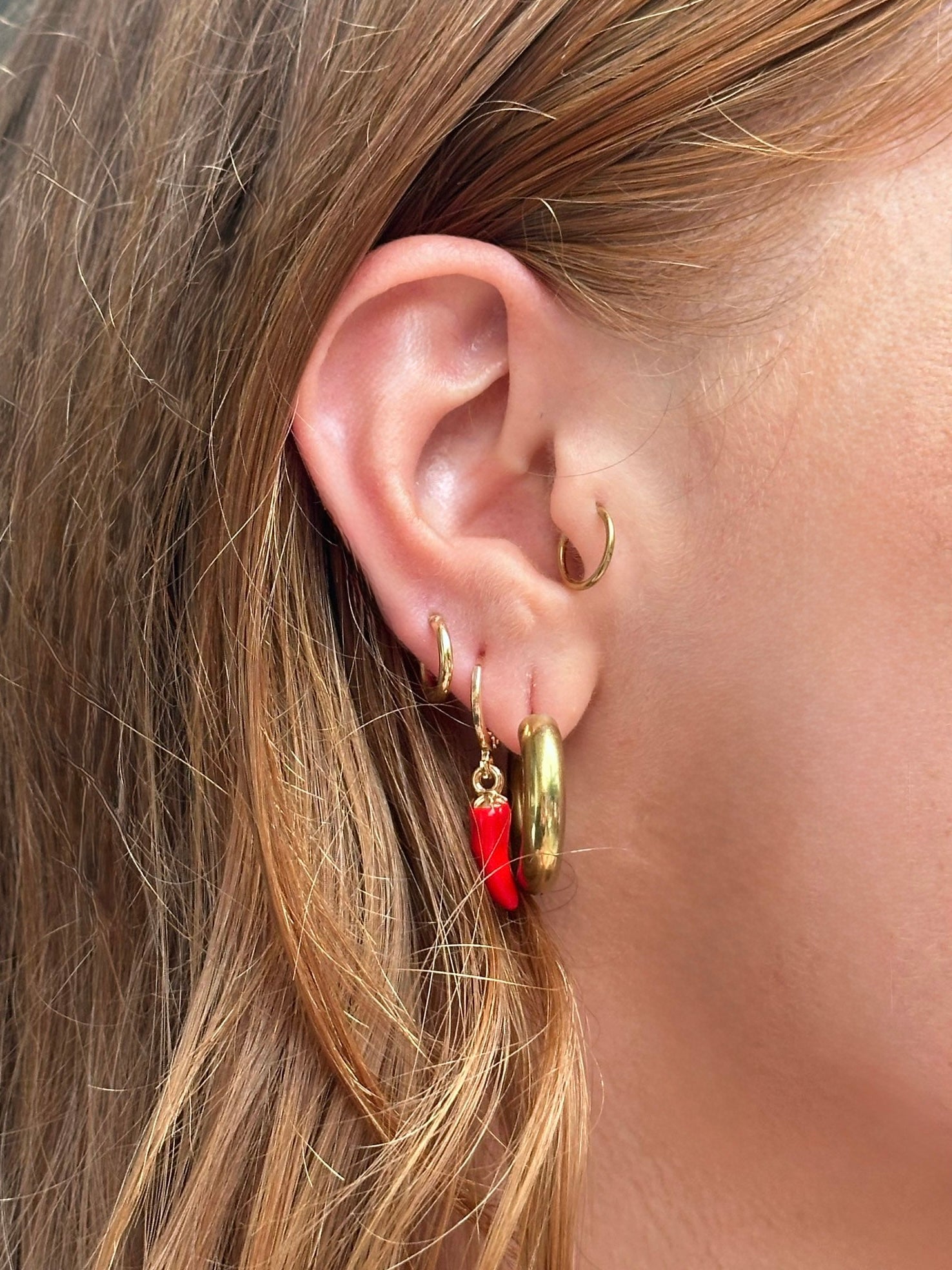 Close-up of an ear wearing gold hoop earrings with a red accent.