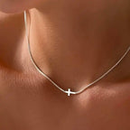 Silver chain necklace with a cross pendant on a person's neck.
