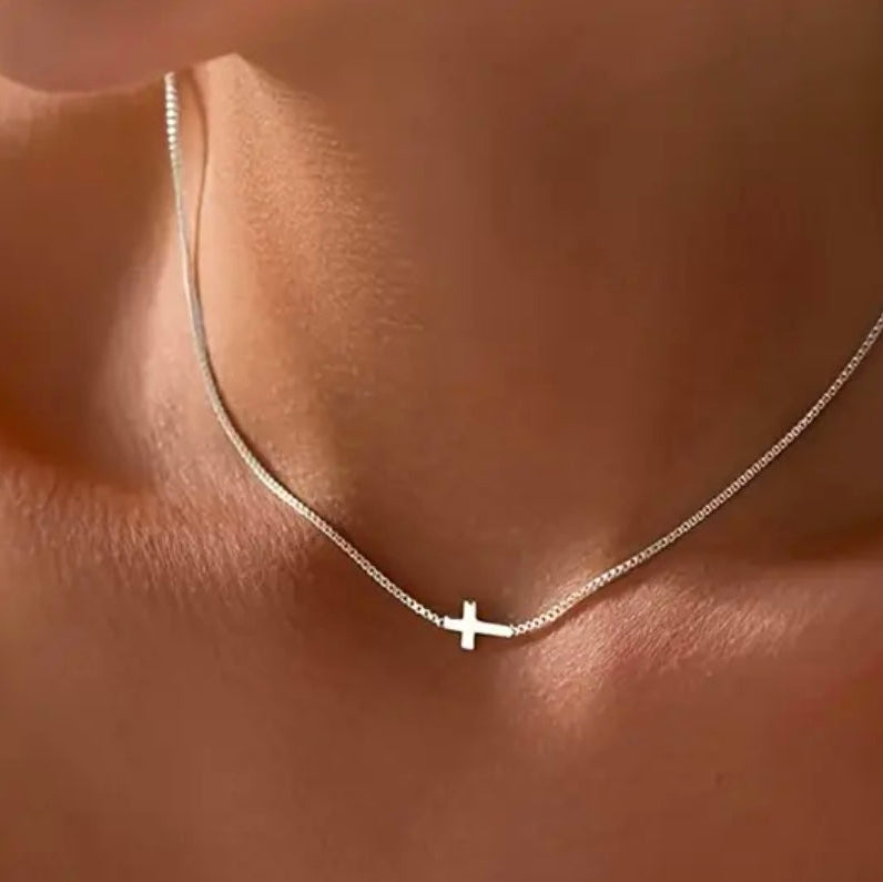 Silver chain necklace with a cross pendant on a person's neck.