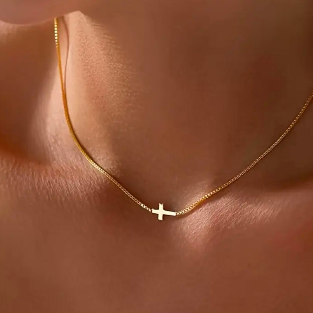 Gold chain necklace with a small cross charm on a person's neck.