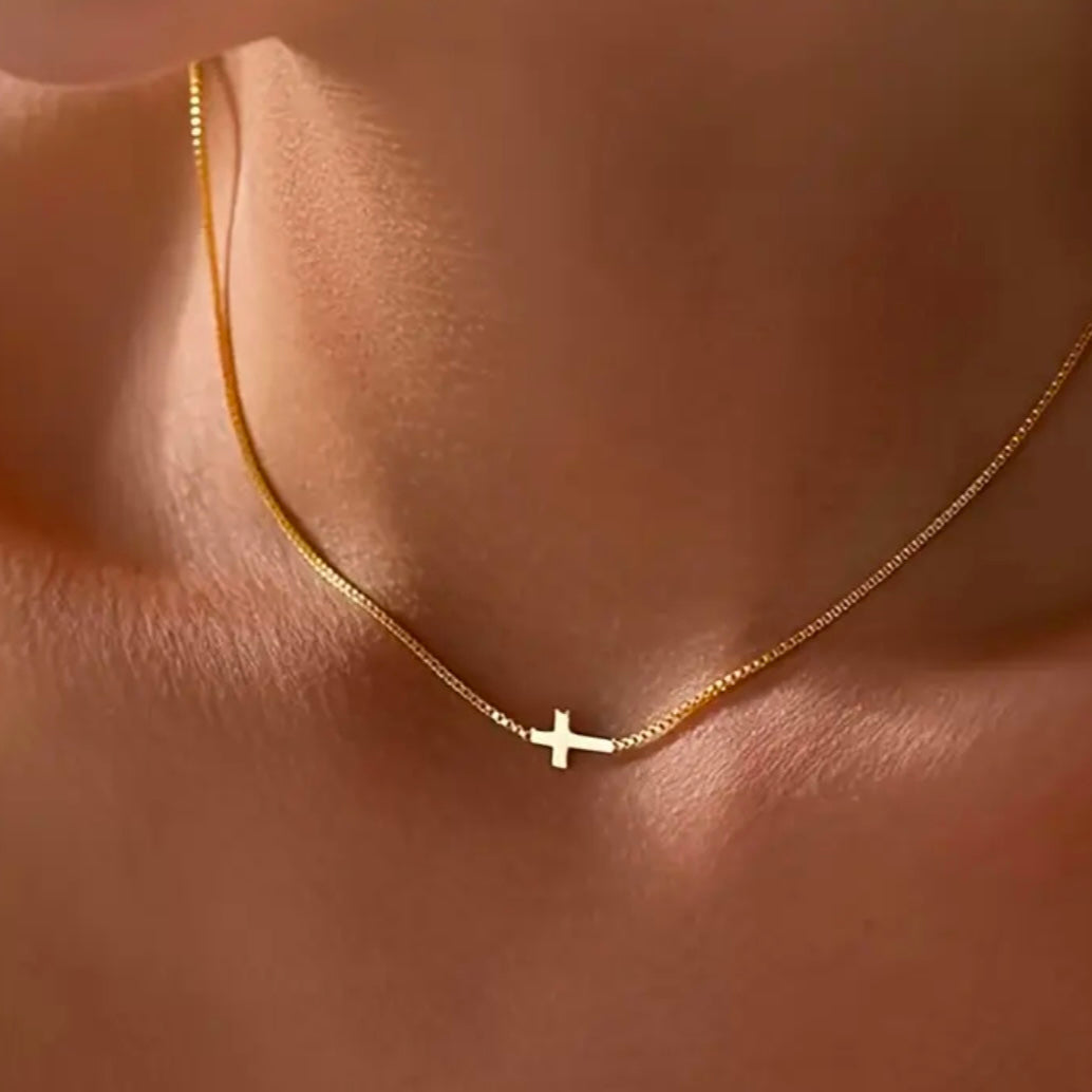 Gold chain necklace with a small cross charm on a person's neck.
