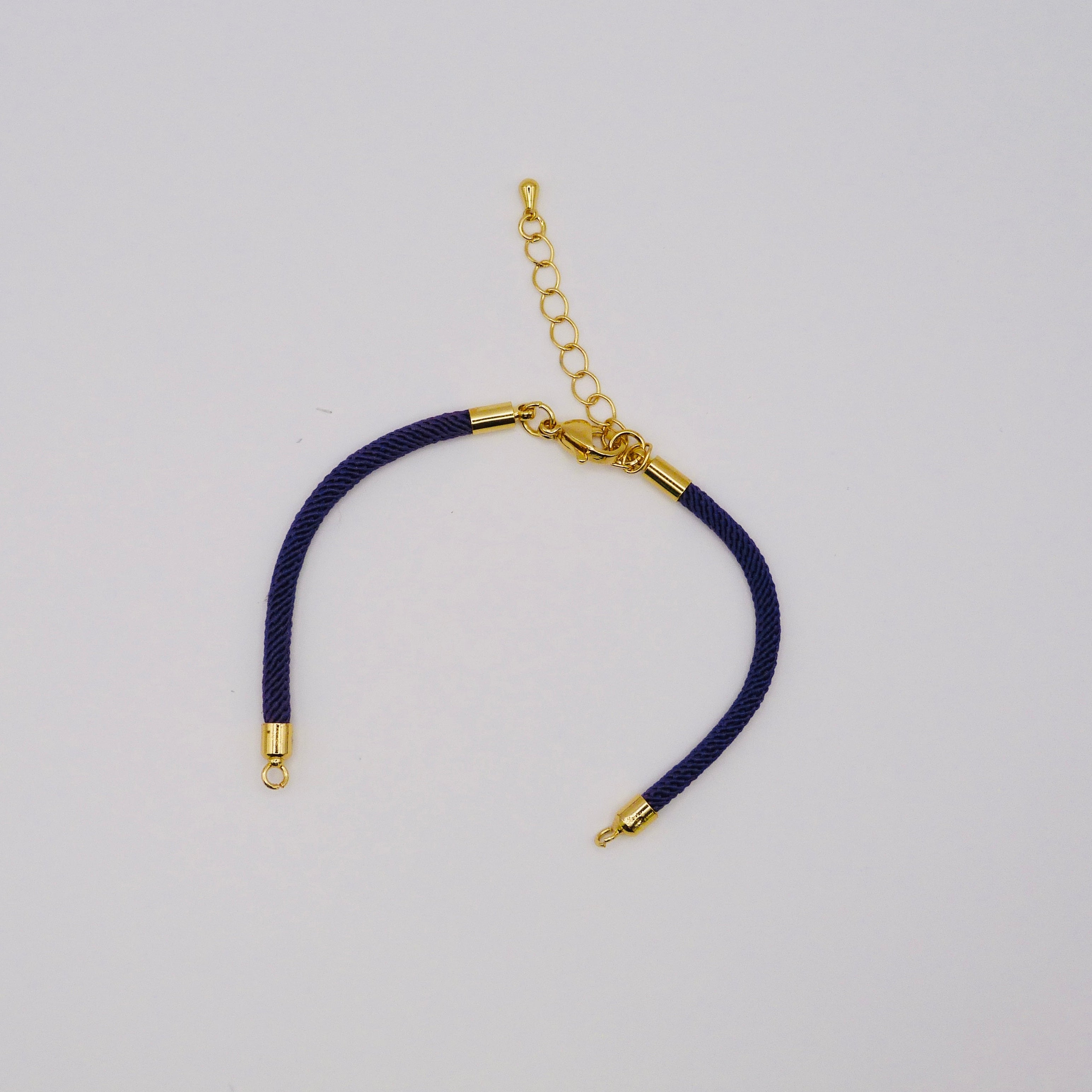 Navy blue cord bracelet with gold clasp on a light gray background