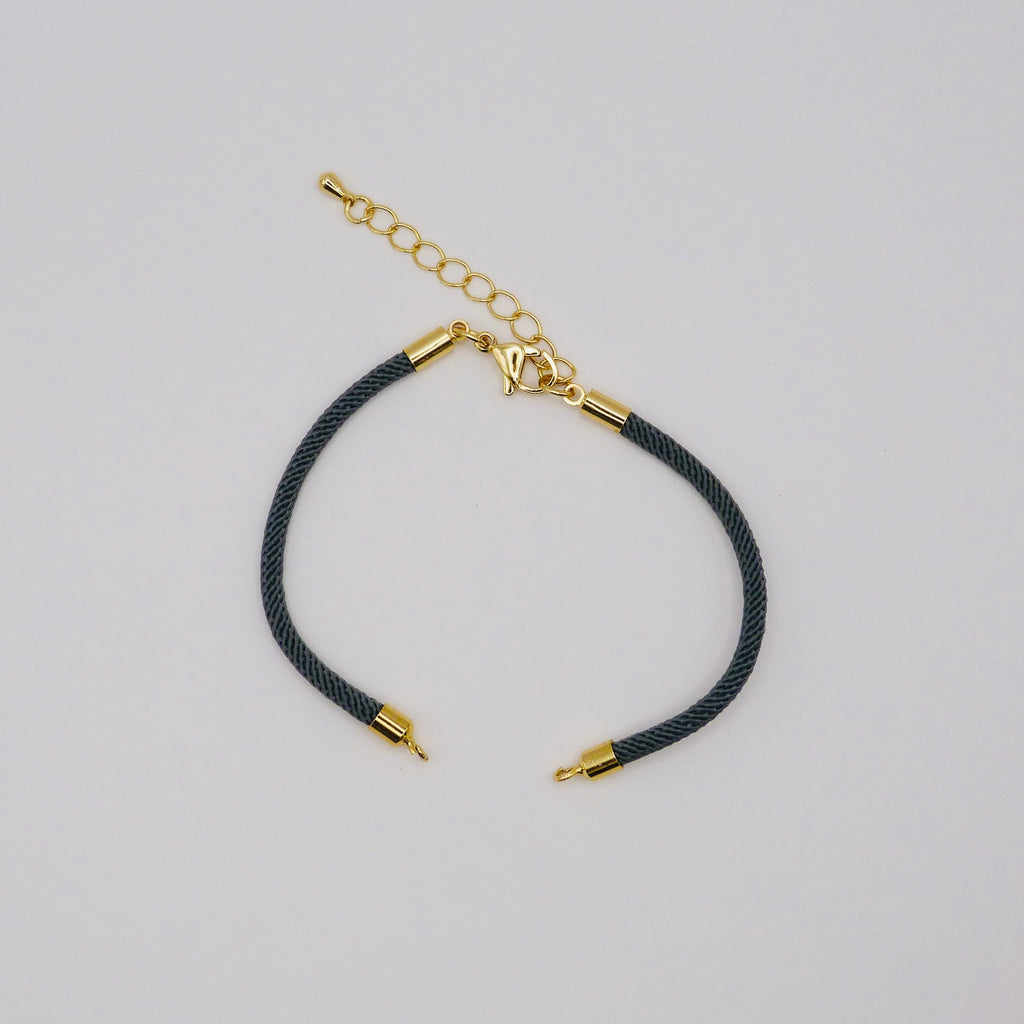 Black cord bracelet with gold accents on a light gray background