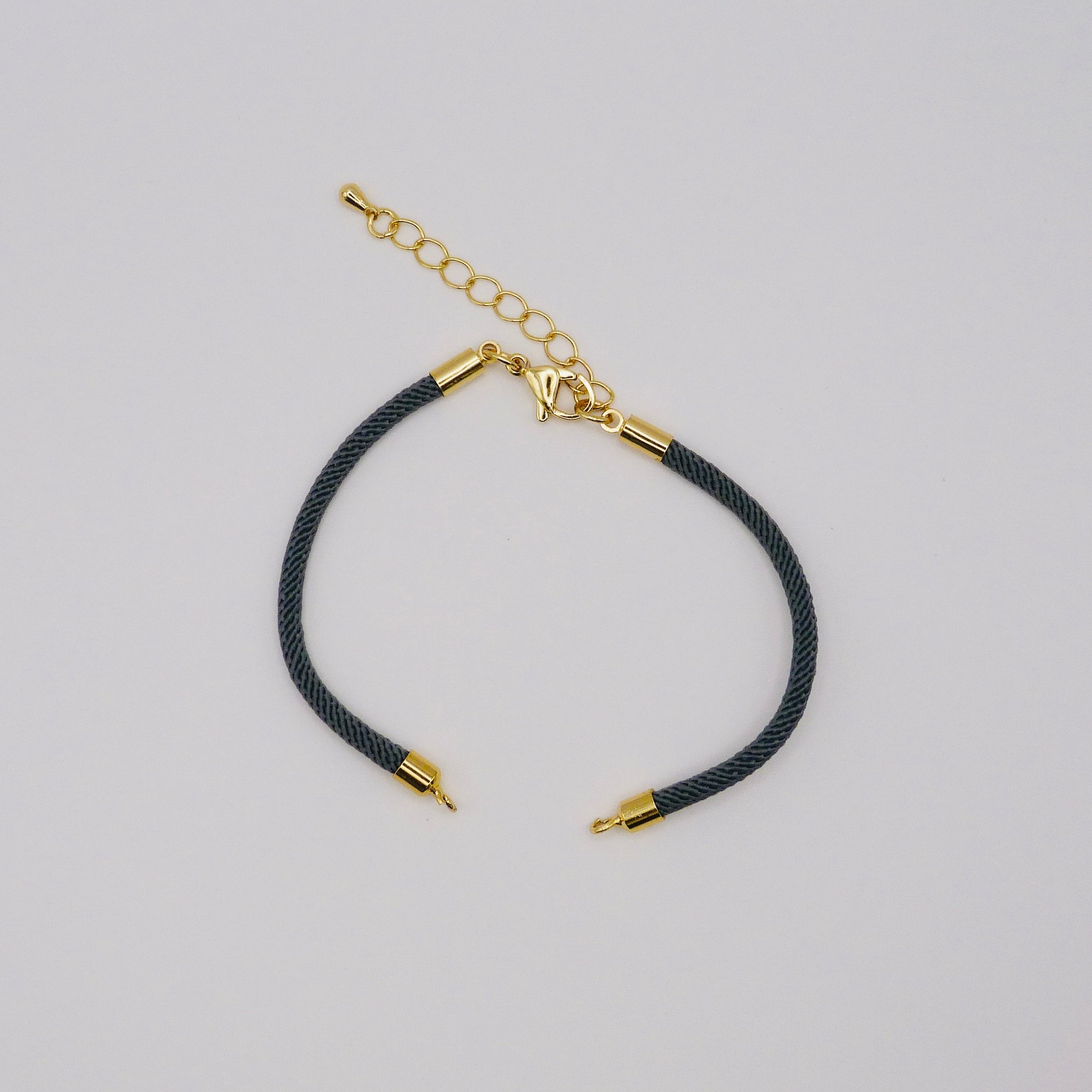 Black cord bracelet with gold accents on a light gray background