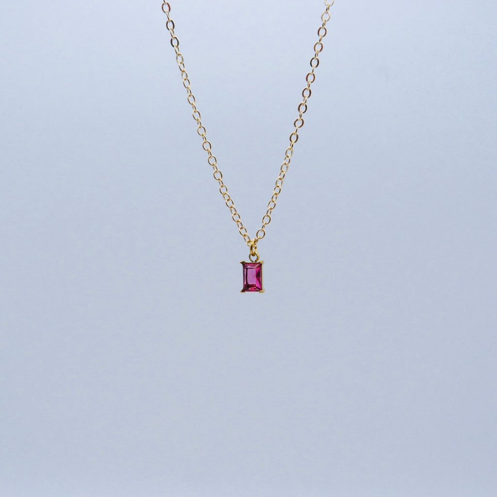 Gold necklace with a pink gemstone pendant on a light gray background