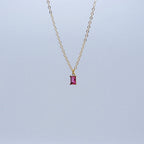 Gold necklace with a pink gemstone pendant on a light gray background