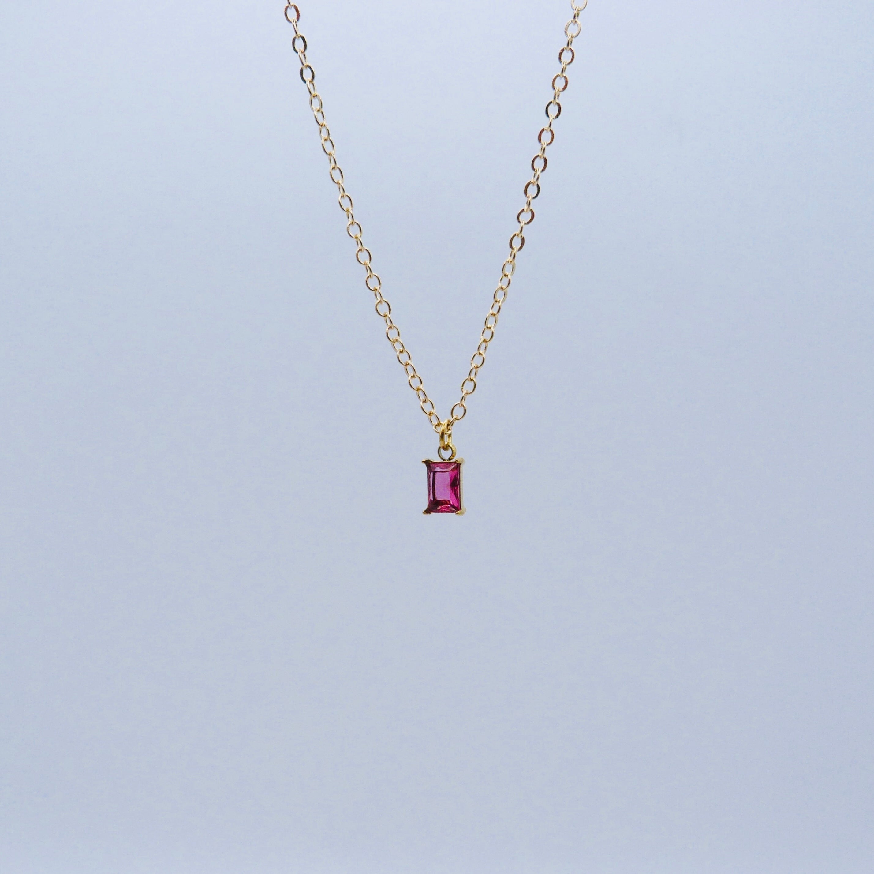 Gold necklace with a pink gemstone pendant on a light gray background
