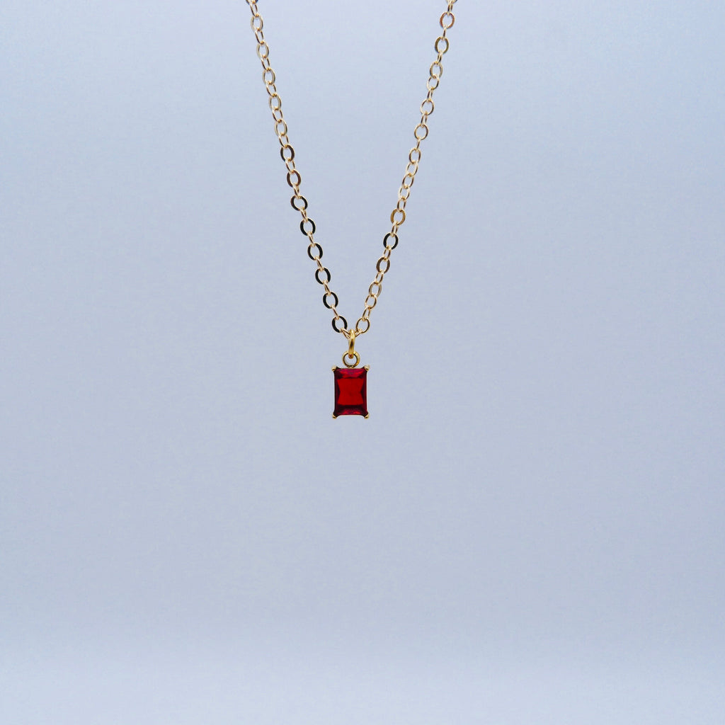 Gold necklace with a red pendant on a light blue background