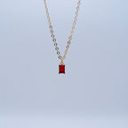 Gold necklace with a red pendant on a light blue background