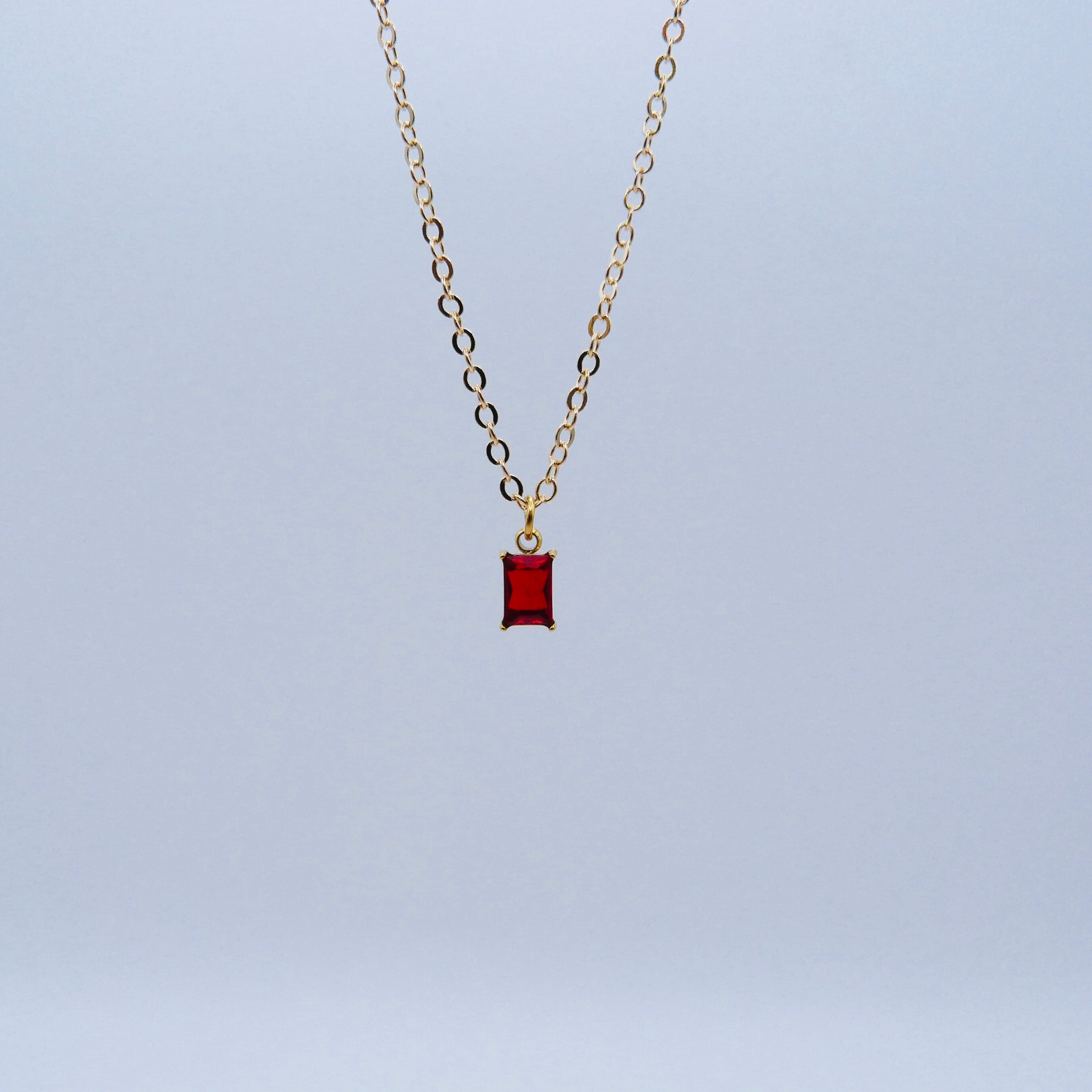Gold necklace with a red pendant on a light blue background