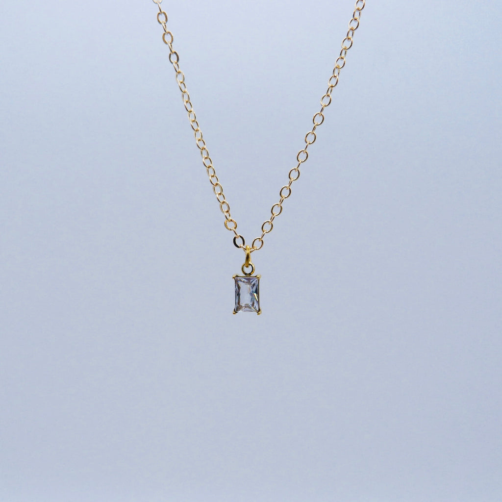 Gold necklace with a rectangular pendant on a light gray background