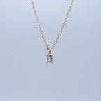 Gold necklace with a rectangular pendant on a light gray background