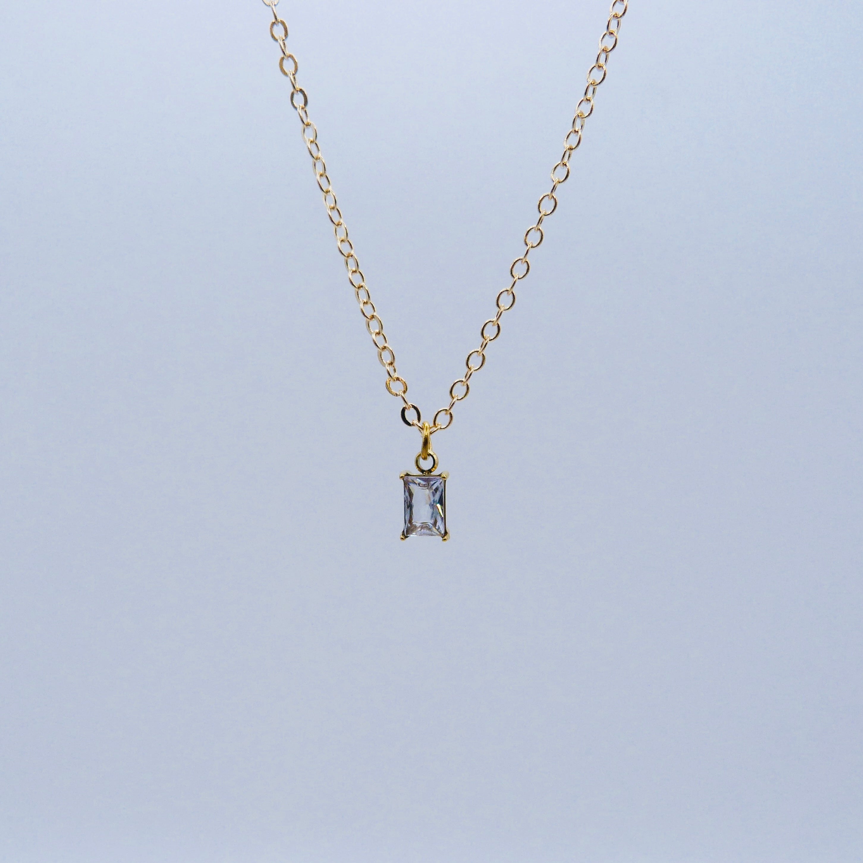 Gold necklace with a rectangular pendant on a light gray background