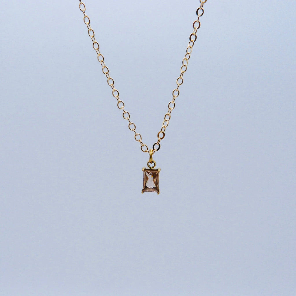 Gold necklace with a baby pink rectangular pendant on a light blue background