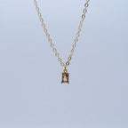 Gold necklace with a baby pink rectangular pendant on a light blue background