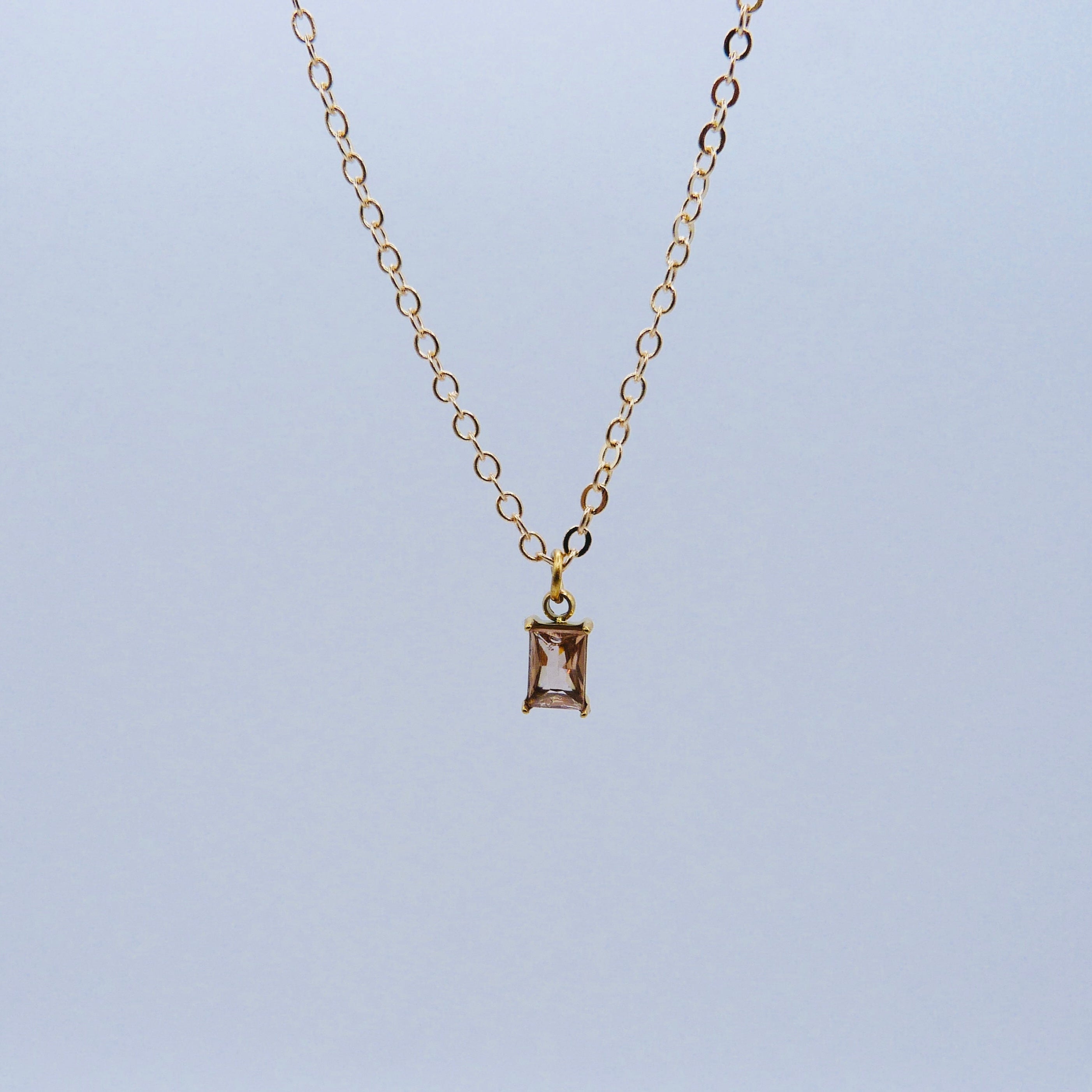 Gold necklace with a baby pink rectangular pendant on a light blue background