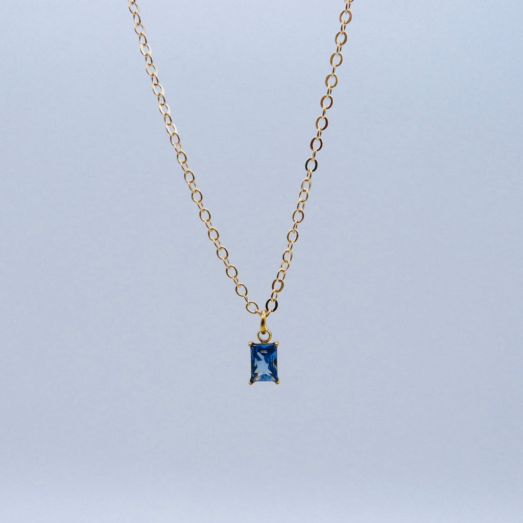 Gold necklace with a blue gemstone pendant on a light gray background