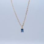 Gold necklace with a blue gemstone pendant on a light gray background