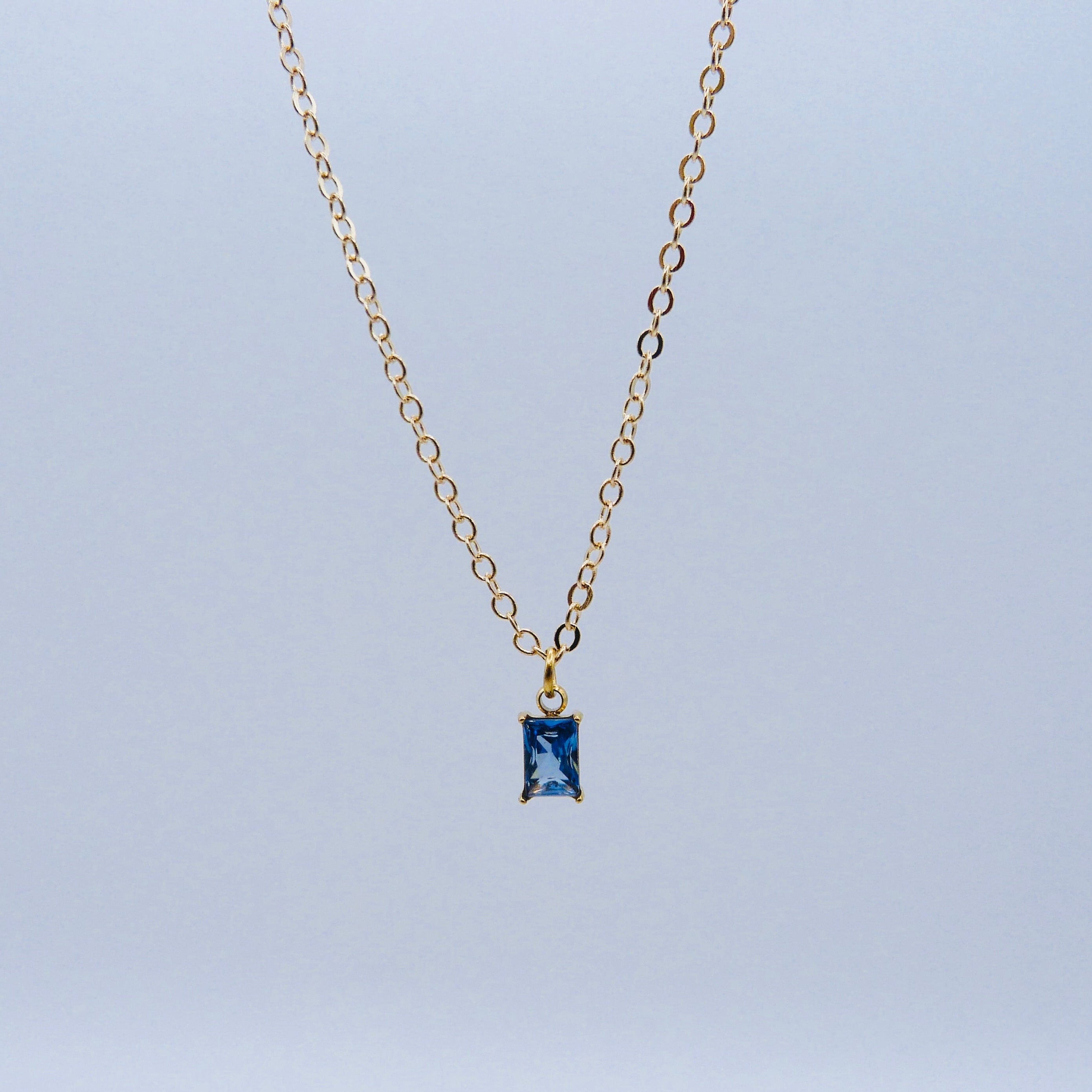 Gold necklace with a blue gemstone pendant on a light gray background