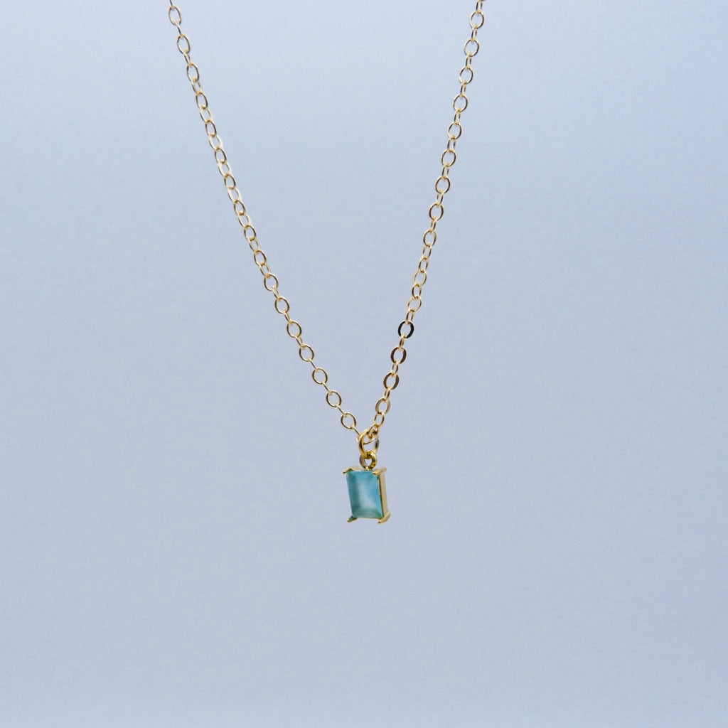 Gold necklace with a smoky blue gemstone pendant on a light gray background