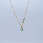 Gold necklace with a smoky blue gemstone pendant on a light gray background