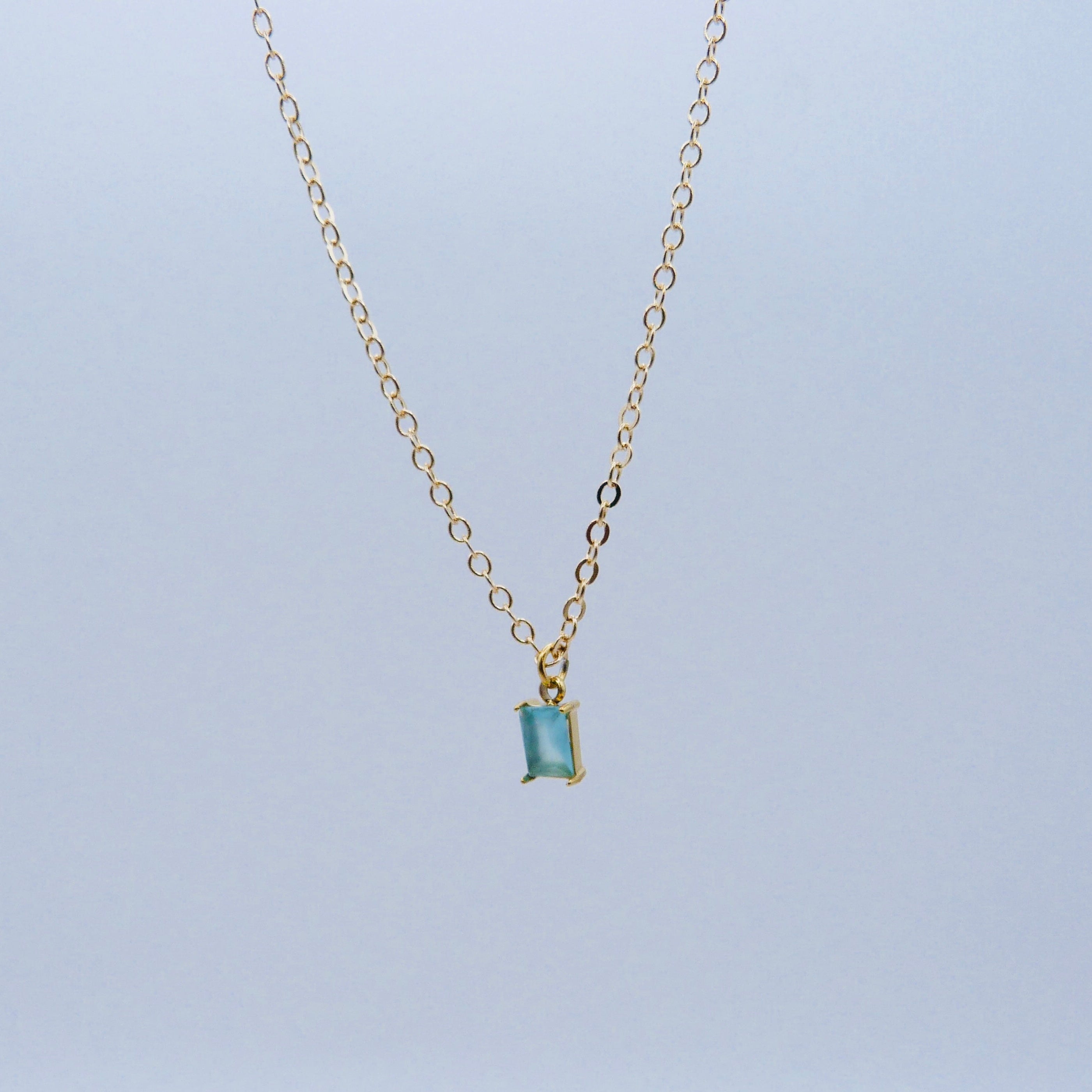 Gold necklace with a smoky blue gemstone pendant on a light gray background