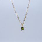 Gold necklace with a green gemstone pendant on a light blue background