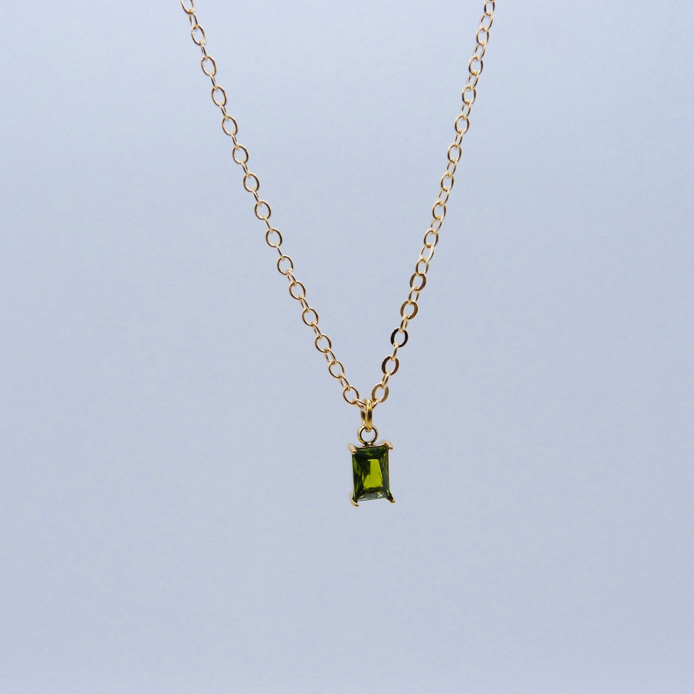 Gold necklace with a green gemstone pendant on a light blue background