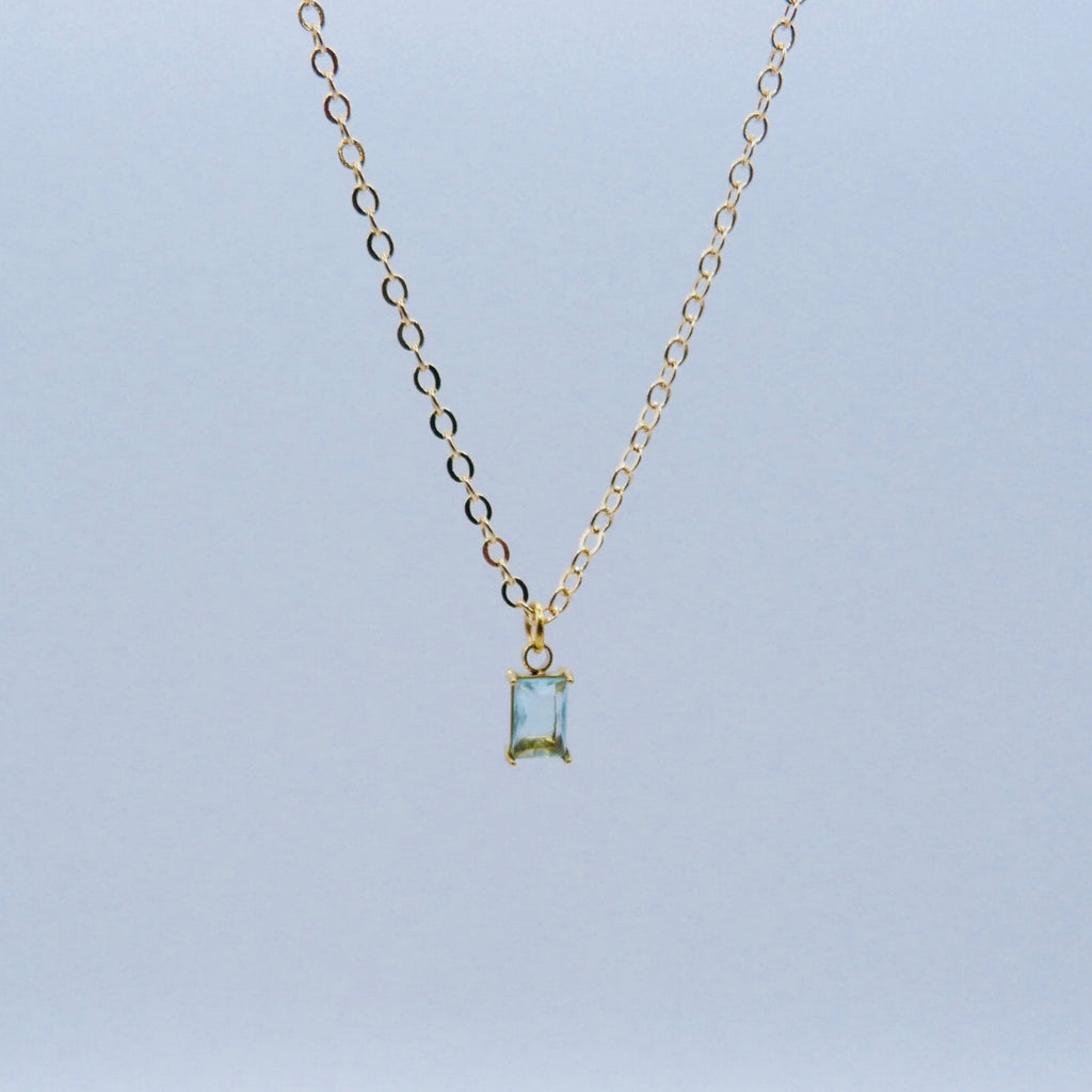 Gold necklace with a rectangular pendant on a light blue background