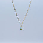 Gold necklace with a rectangular pendant on a light blue background