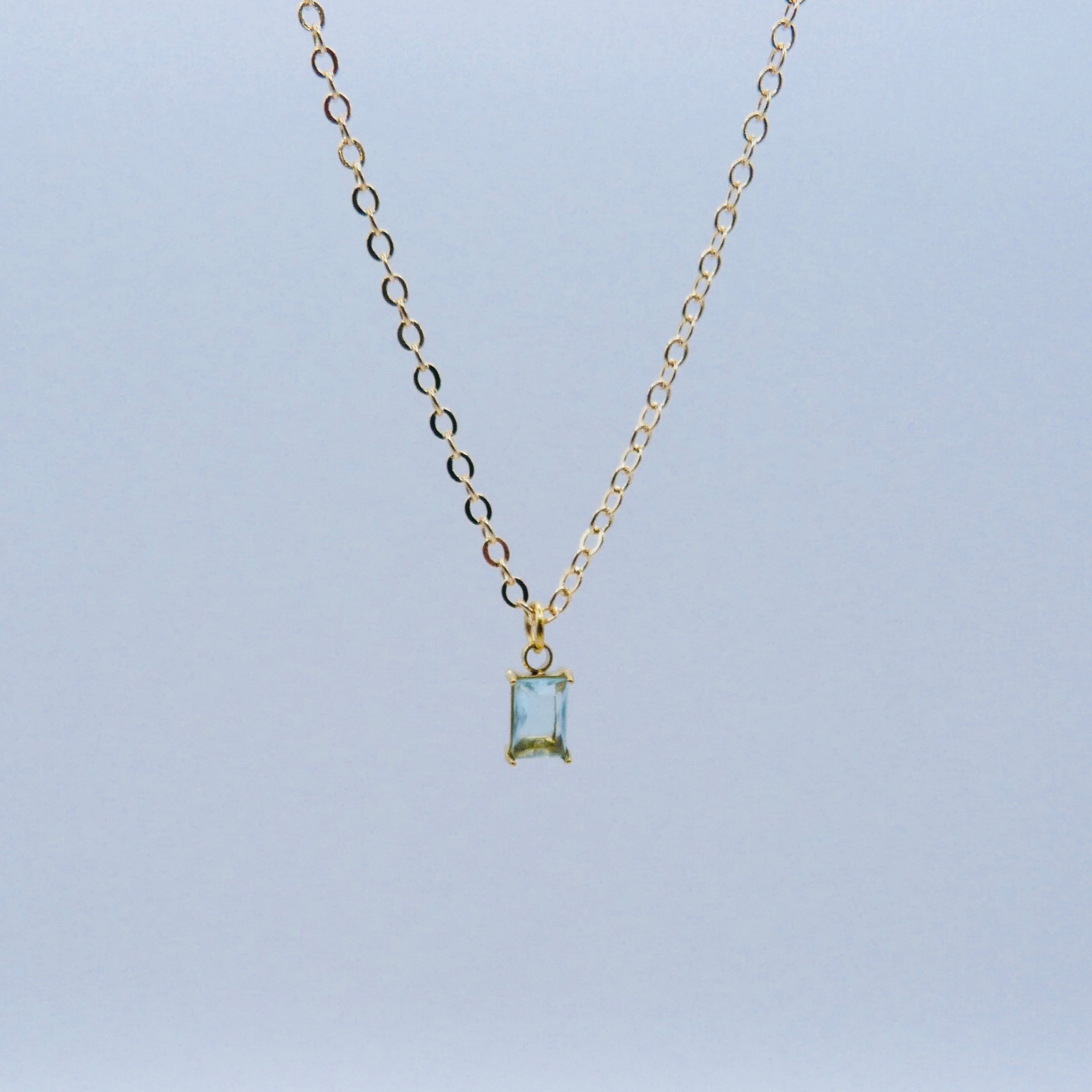 Gold necklace with a rectangular pendant on a light blue background
