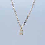 Gold necklace with a rectangular pendant on a light blue background