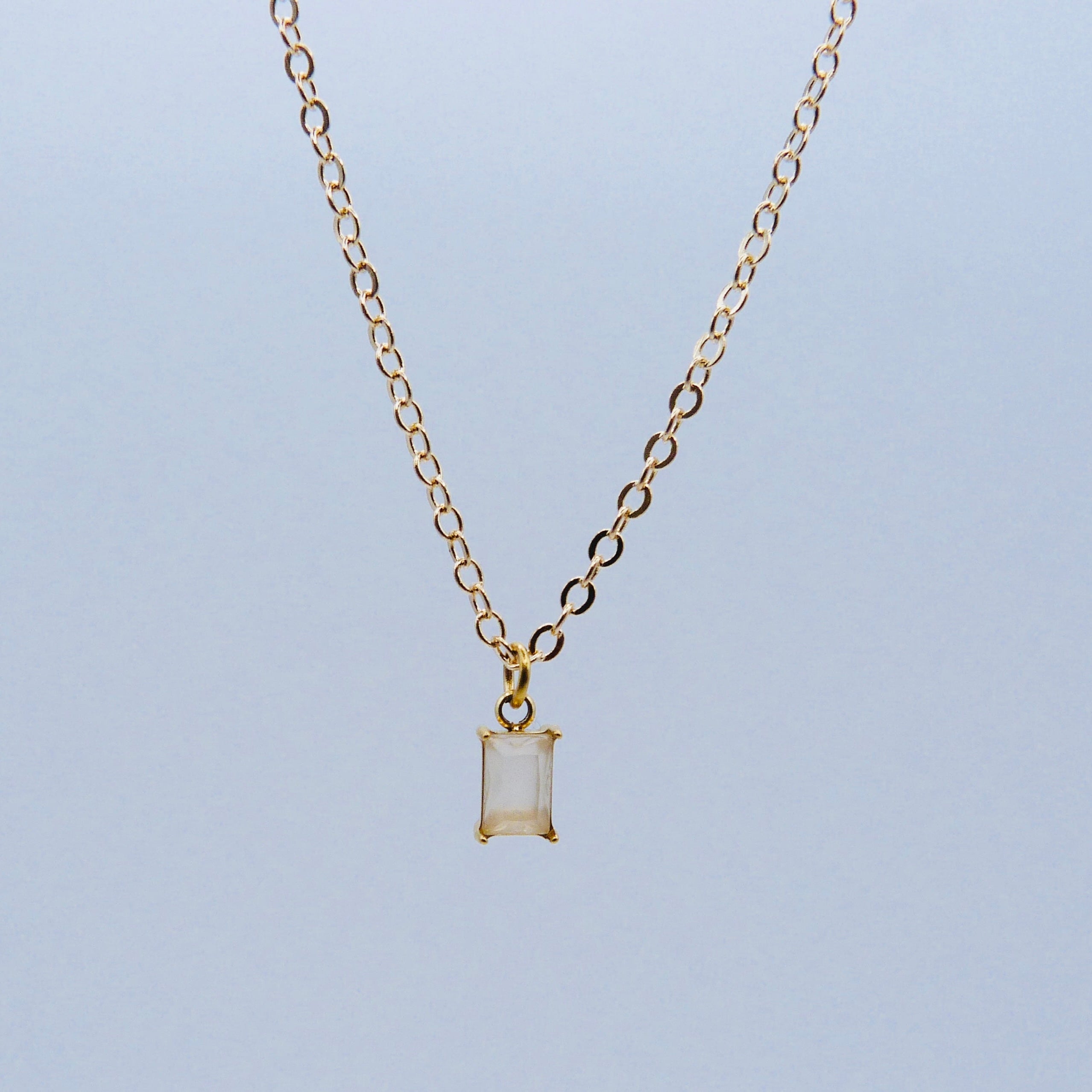 Gold necklace with a rectangular pendant on a light blue background
