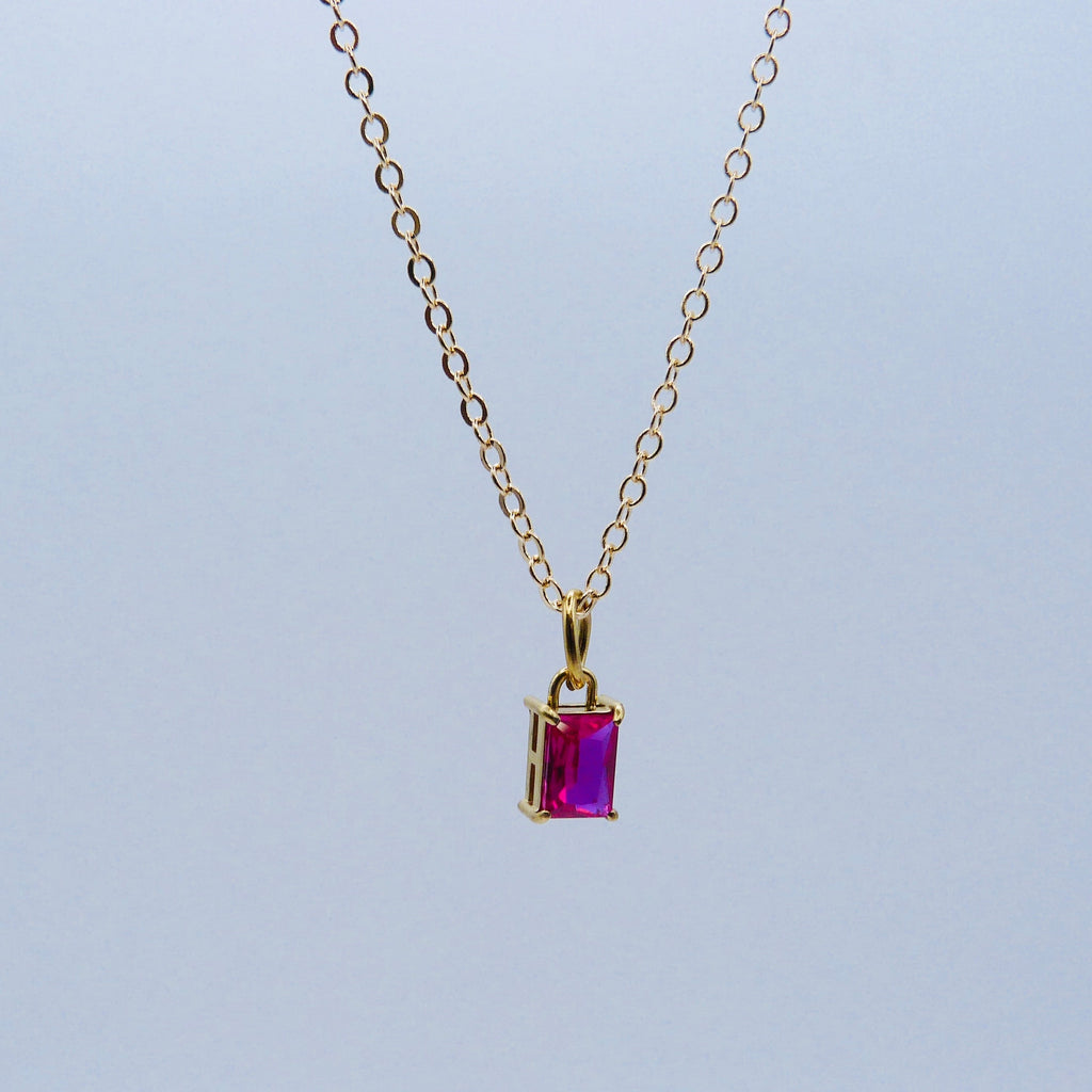 Gold necklace with a purple gemstone pendant on a light gray background