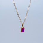 Gold necklace with a purple gemstone pendant on a light gray background