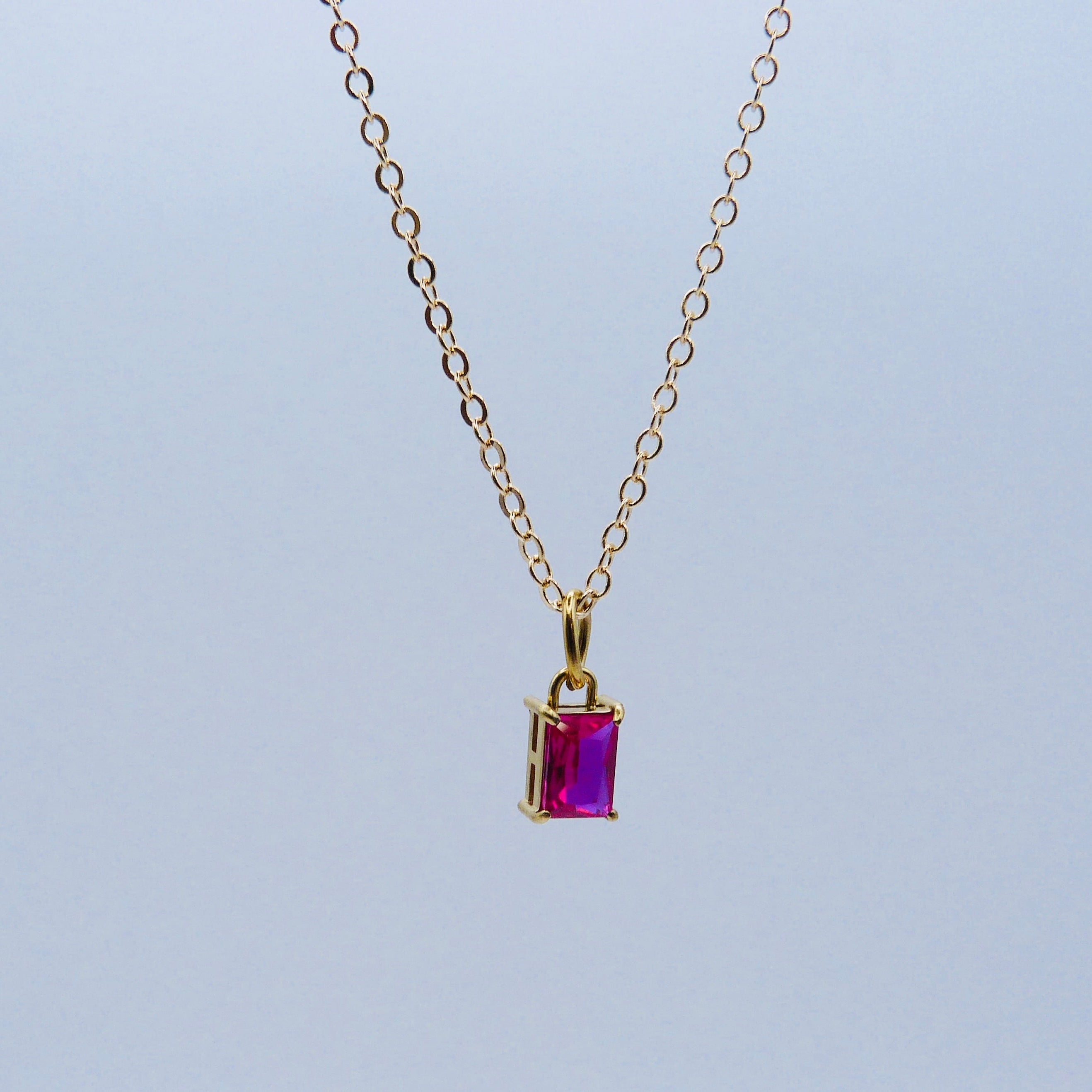 Gold necklace with a purple gemstone pendant on a light gray background
