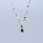 Gold necklace with a purple gemstone pendant on a light blue background