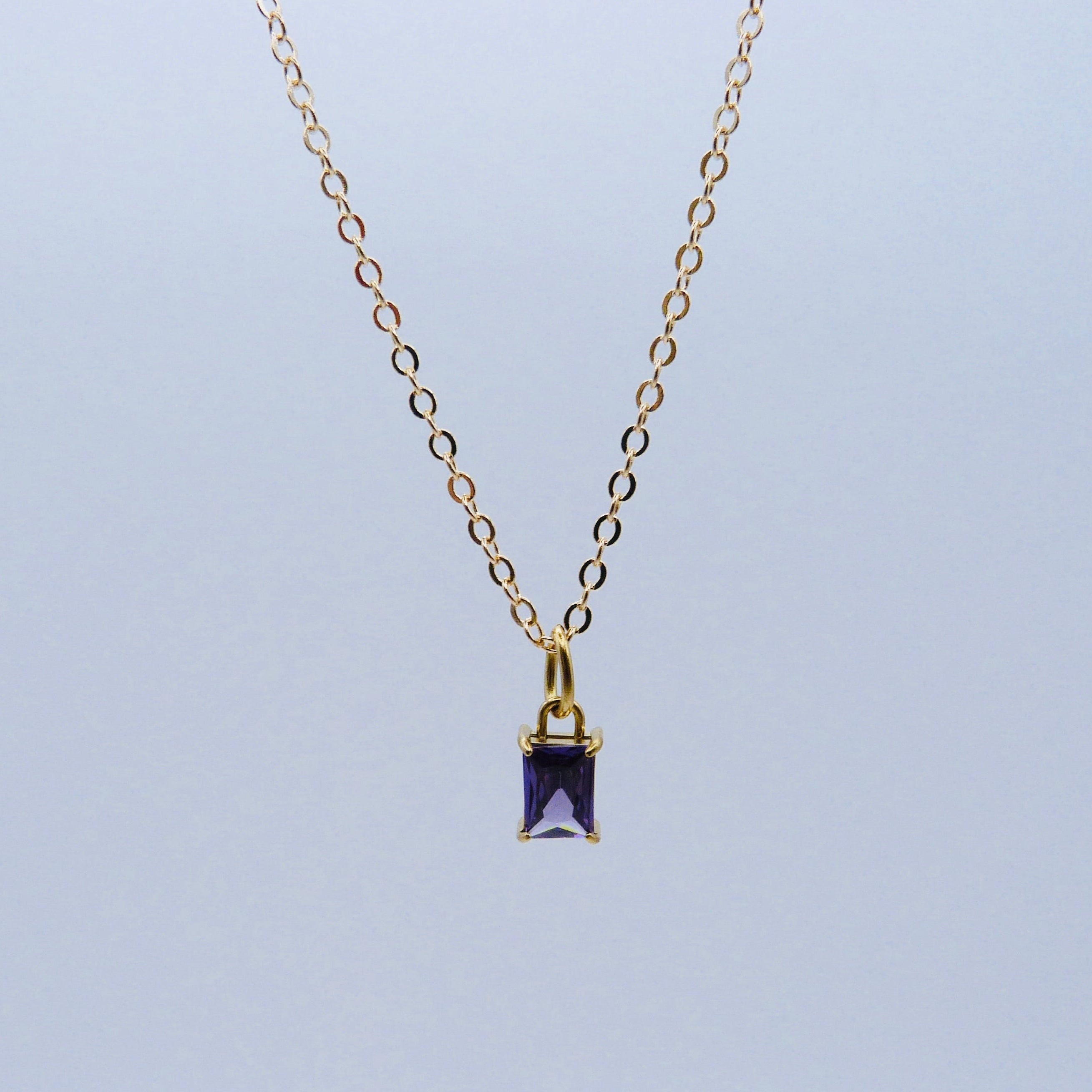 Gold necklace with a purple gemstone pendant on a light blue background