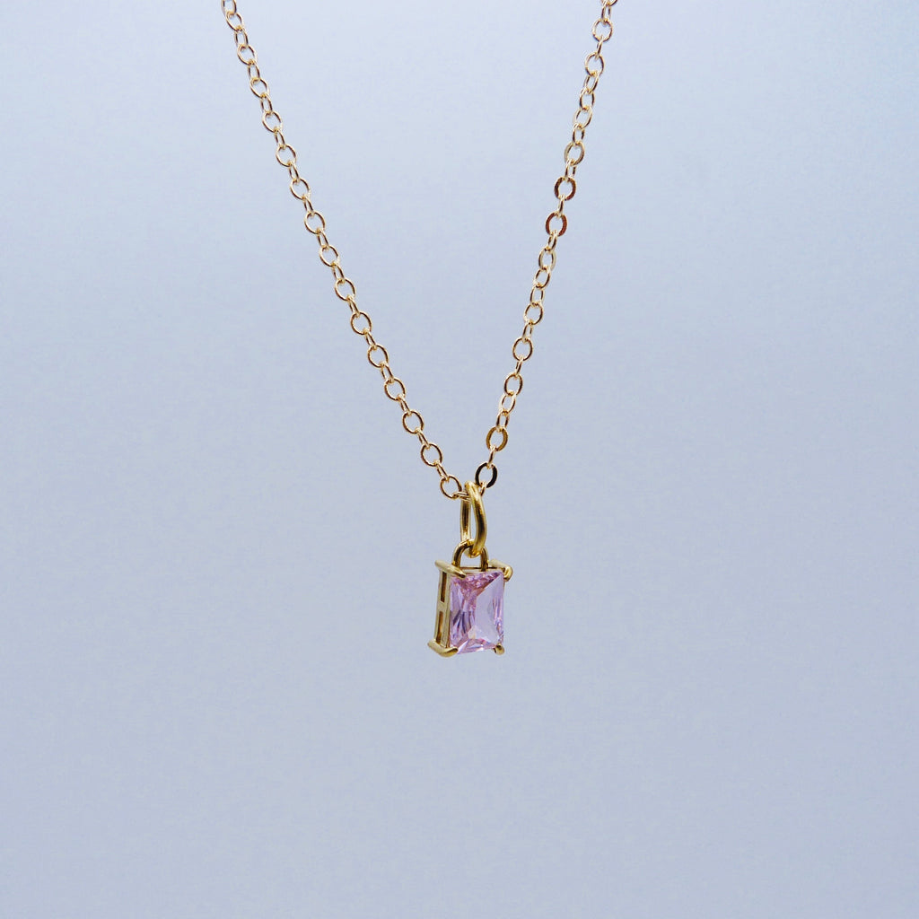 Gold necklace with a purple gemstone pendant on a light gray background