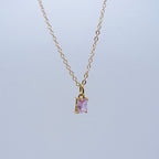 Gold necklace with a purple gemstone pendant on a light gray background