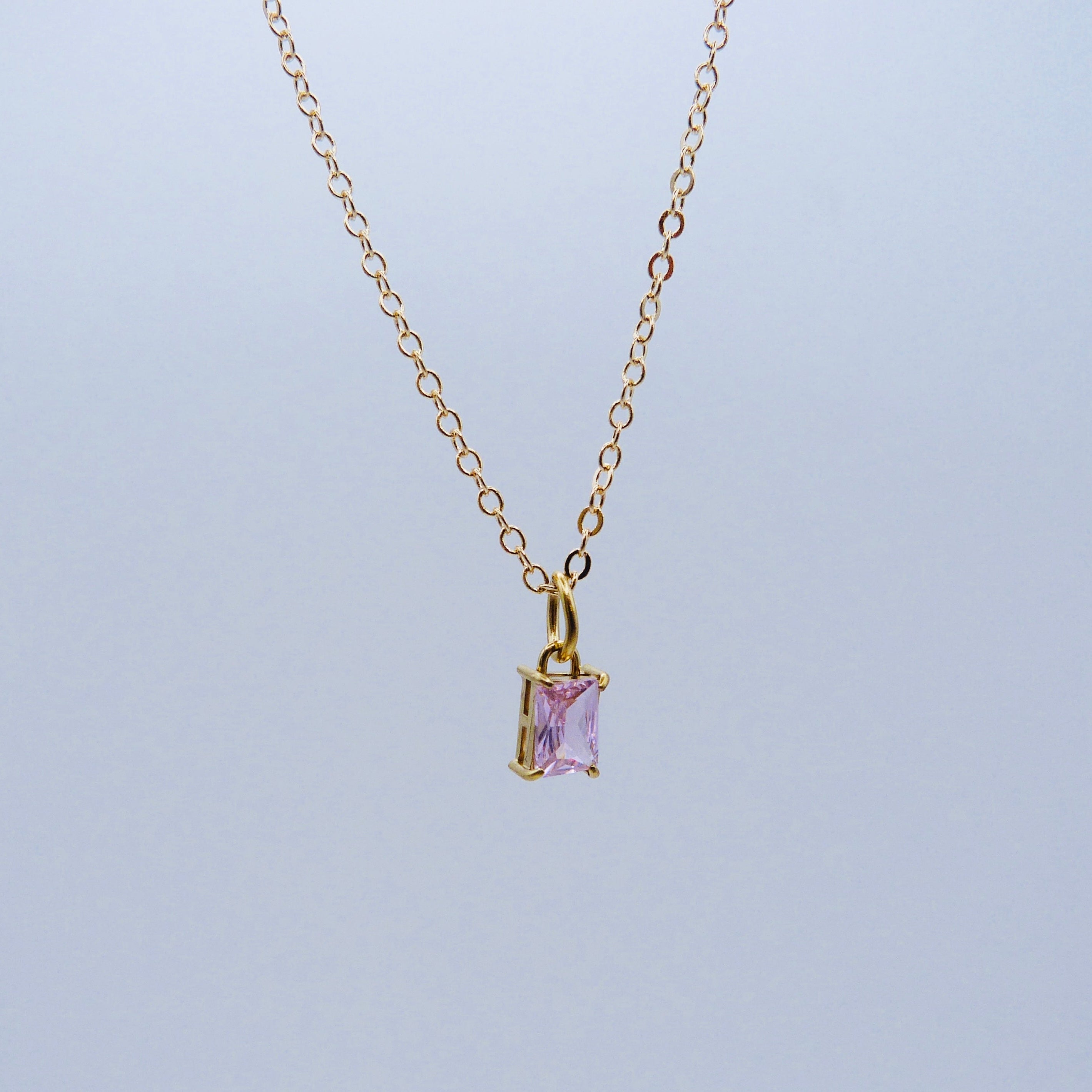 Gold necklace with a purple gemstone pendant on a light gray background