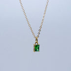 Gold necklace with a green gemstone pendant on a light gray background