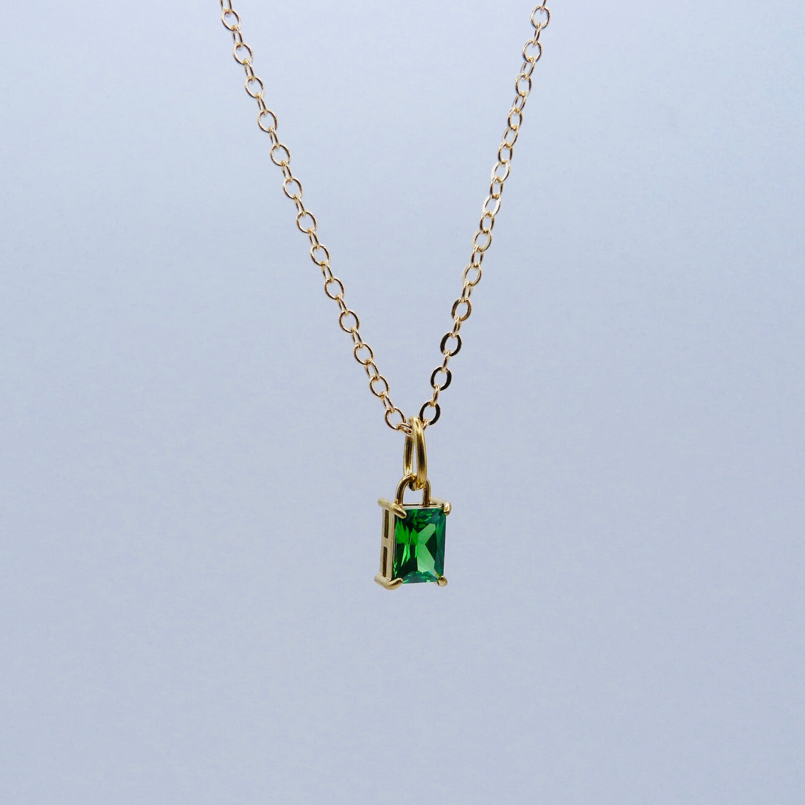 Gold necklace with a green gemstone pendant on a light gray background