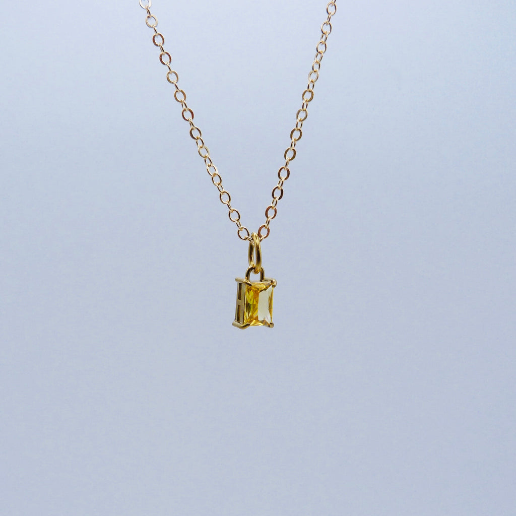Gold necklace with a rectangular yellow gemstone pendant on a light gray background