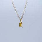Gold necklace with a rectangular yellow gemstone pendant on a light gray background