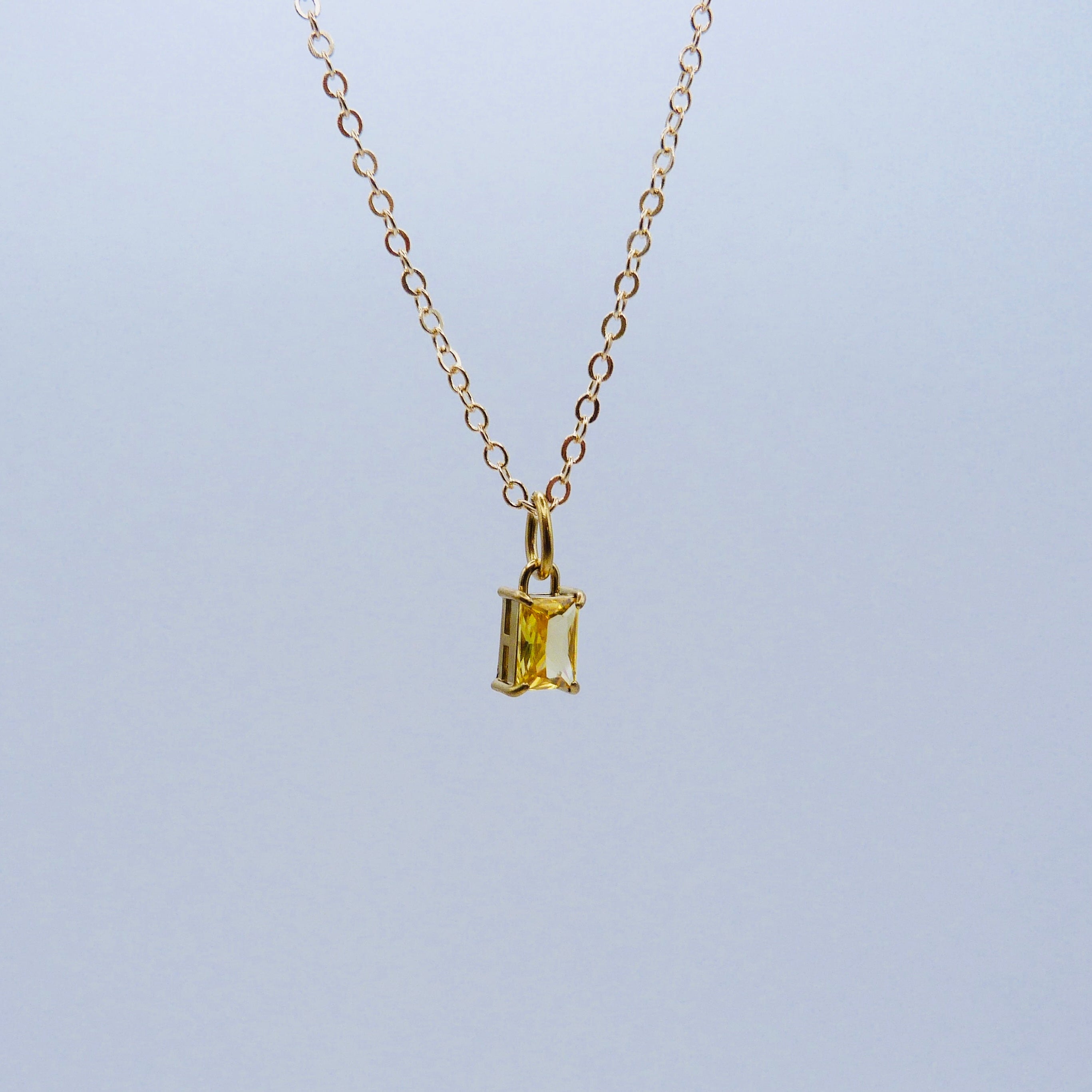 Gold necklace with a rectangular yellow gemstone pendant on a light gray background