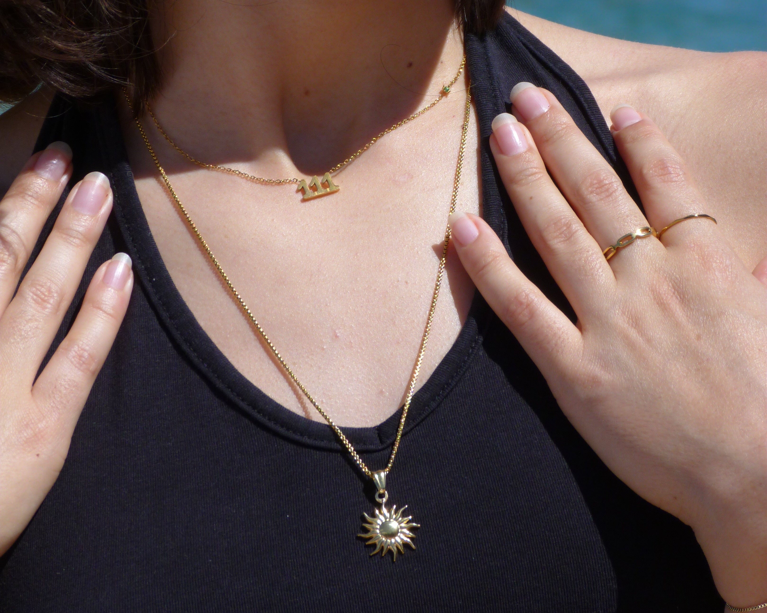 Woman lying down with a hand on her chest and another hand touching her hair, wearing a necklace.