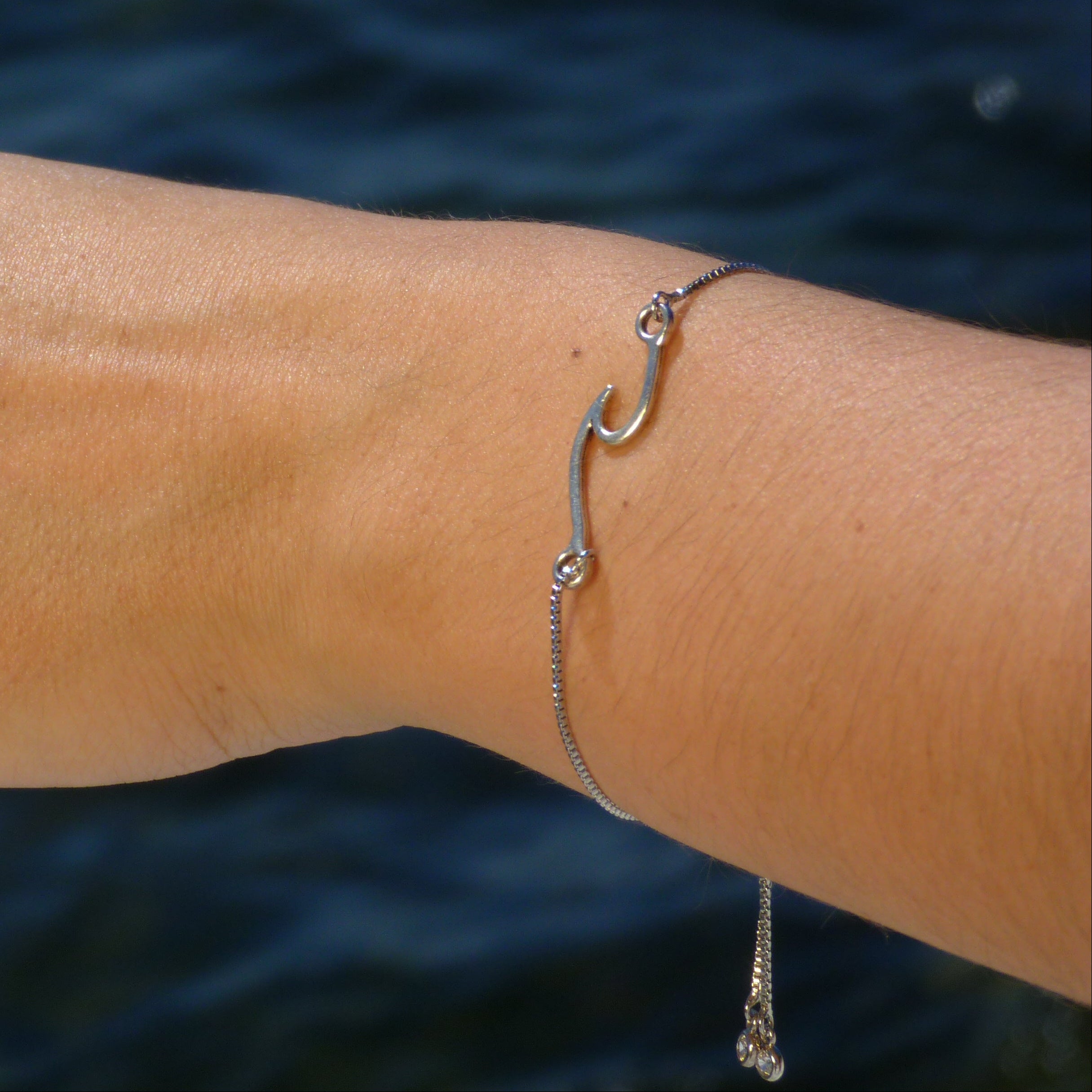 Hand with a ring and bracelet against a blue water background