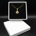 Gold necklace with sun design in a black box on a dark background