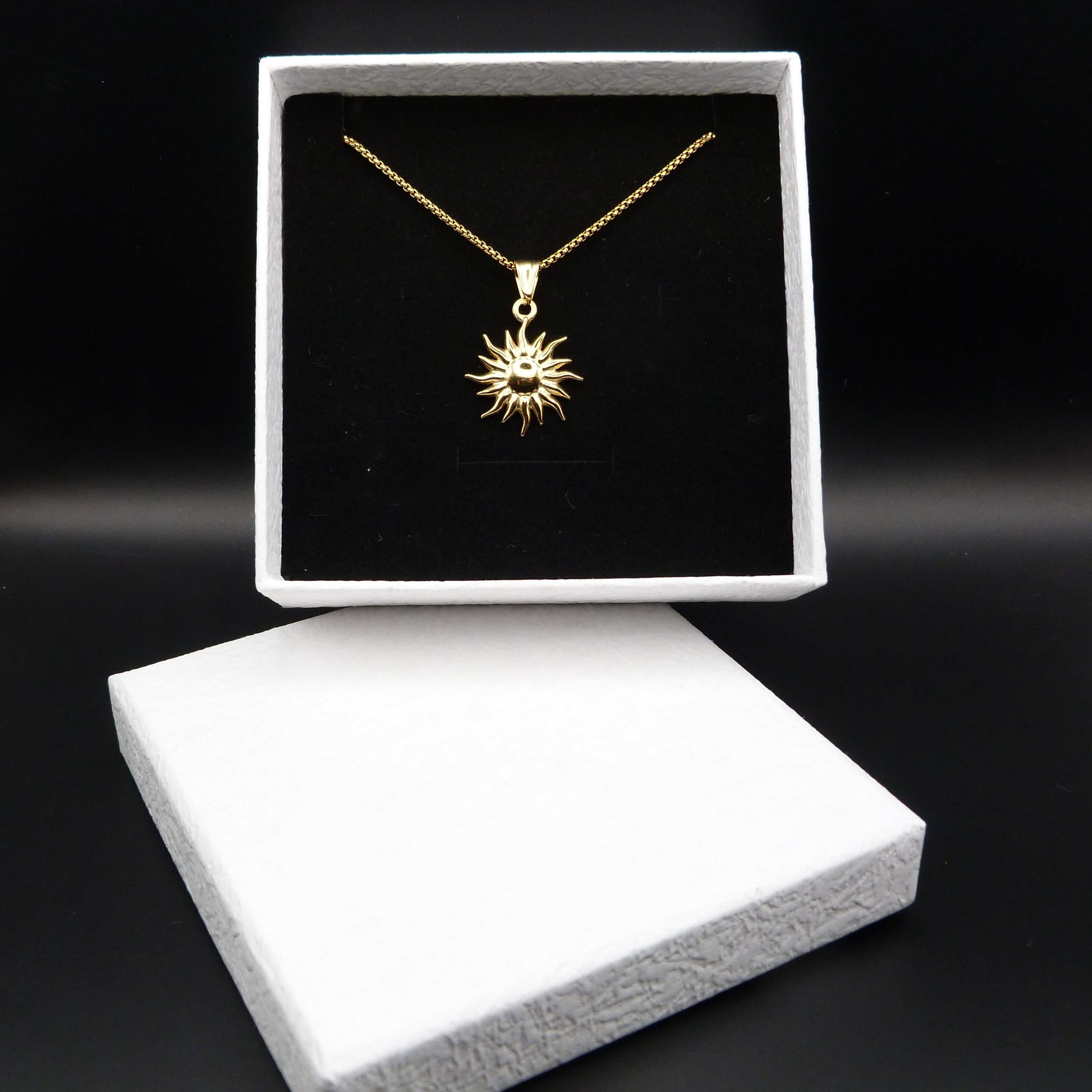 Gold necklace with sun design in a black box on a dark background